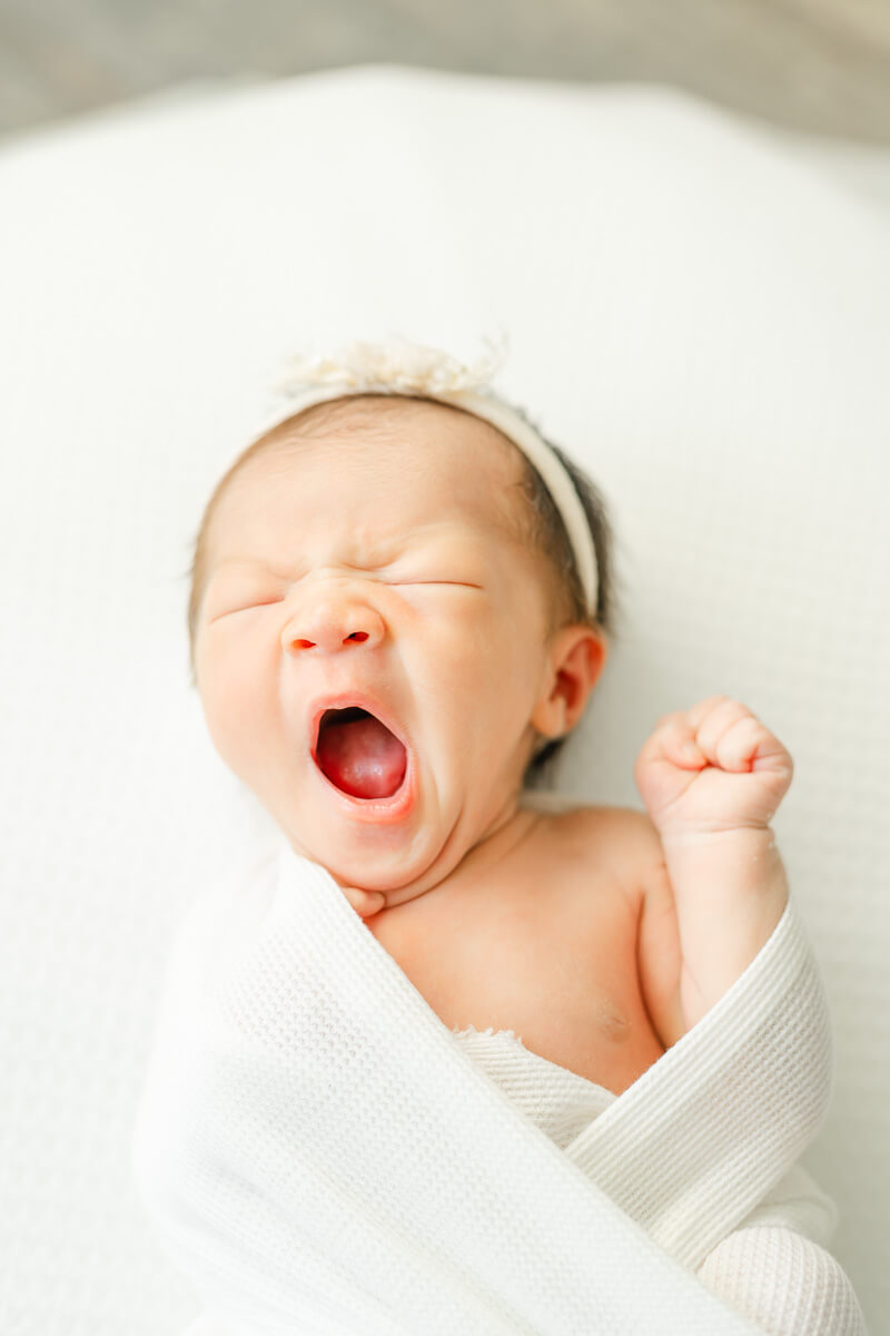 baby wrapped in white blanket yawns in candid photo captured by an Austin newborn photographer.