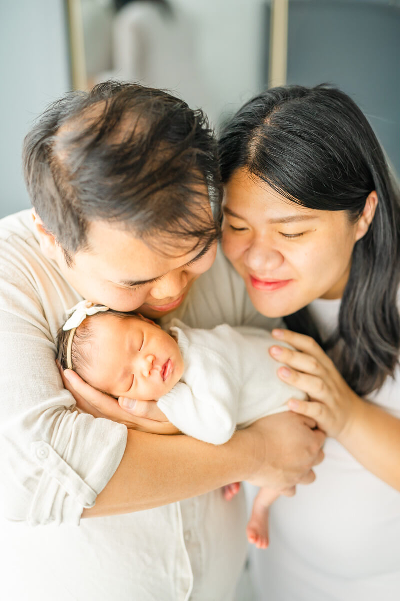 parents snuggle infant girl in posed newborn portrait.