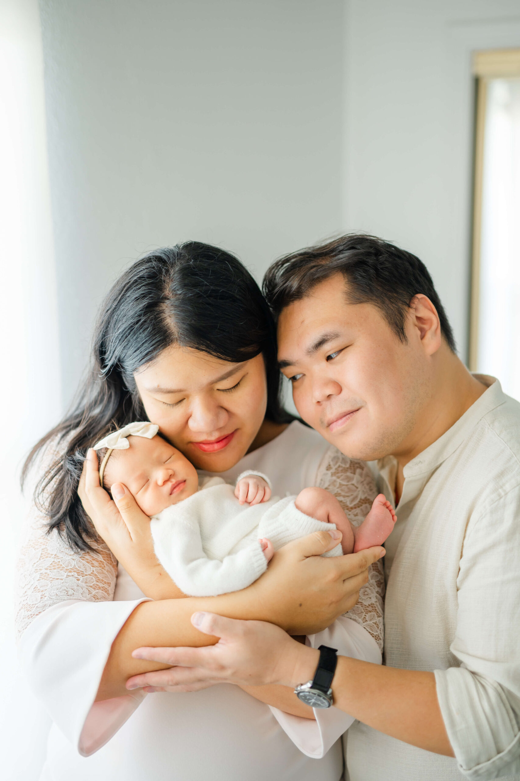Happy new mom and dad snuggle with their sleeping newborn in their hands against mom's cheek after visiting baby boutiques in austin
