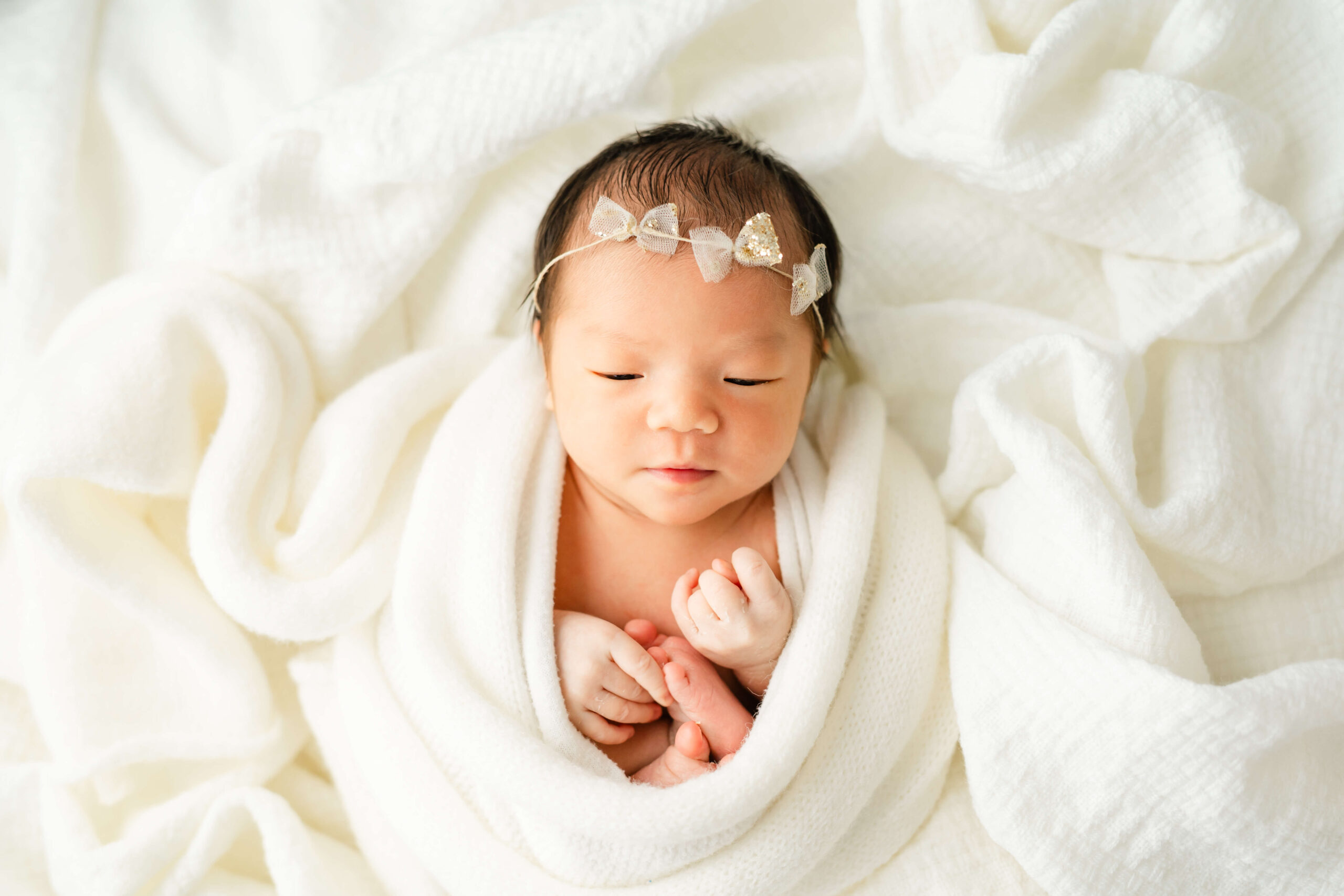 A newborn baby lays in a white swaddle on a bed of blankets with a headband after visiting baby boutiques in austin