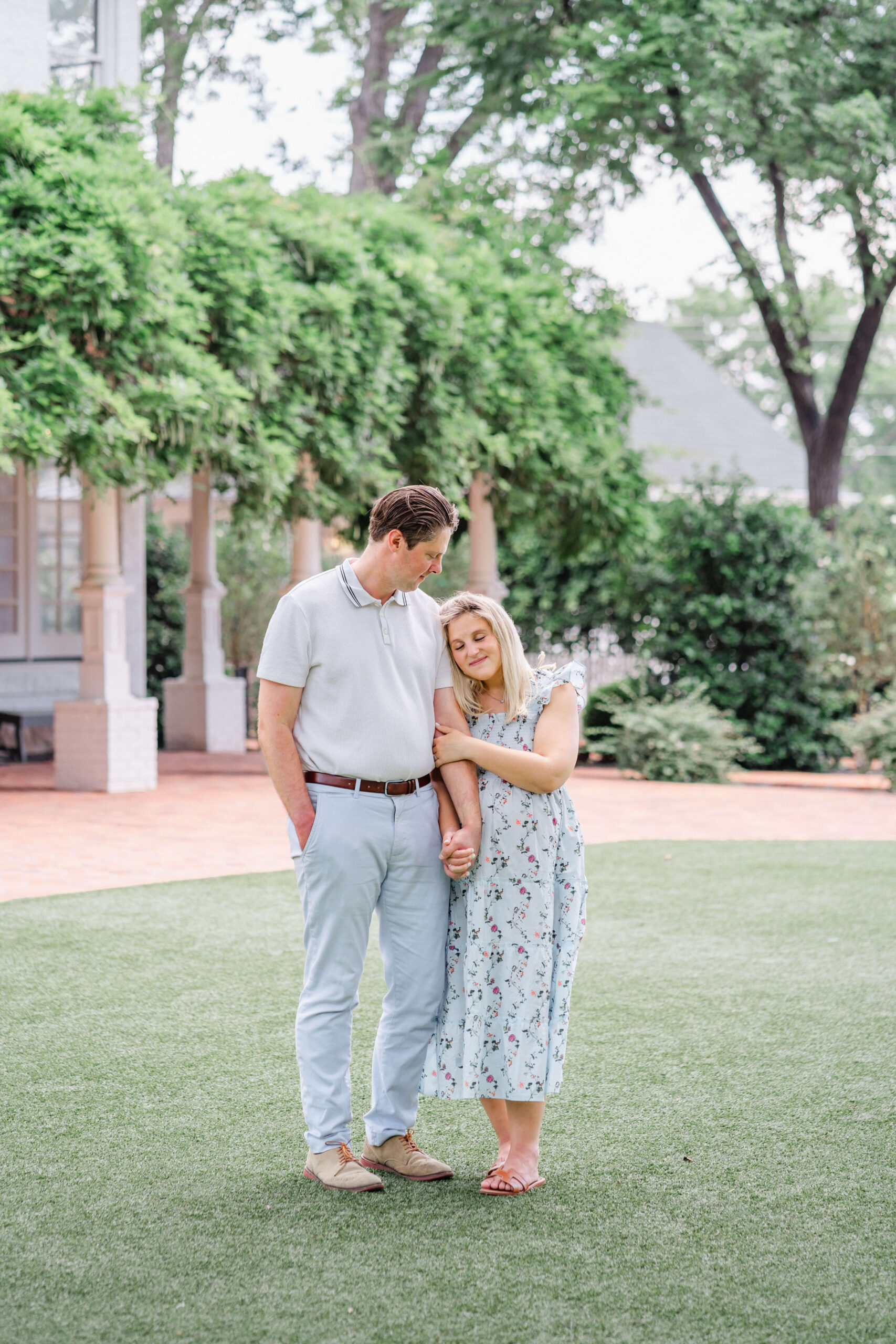 A pregnant woman snuggles on the arm of her husband while holding hands in a garden in a blue maternity dress after meeting midwives in austin