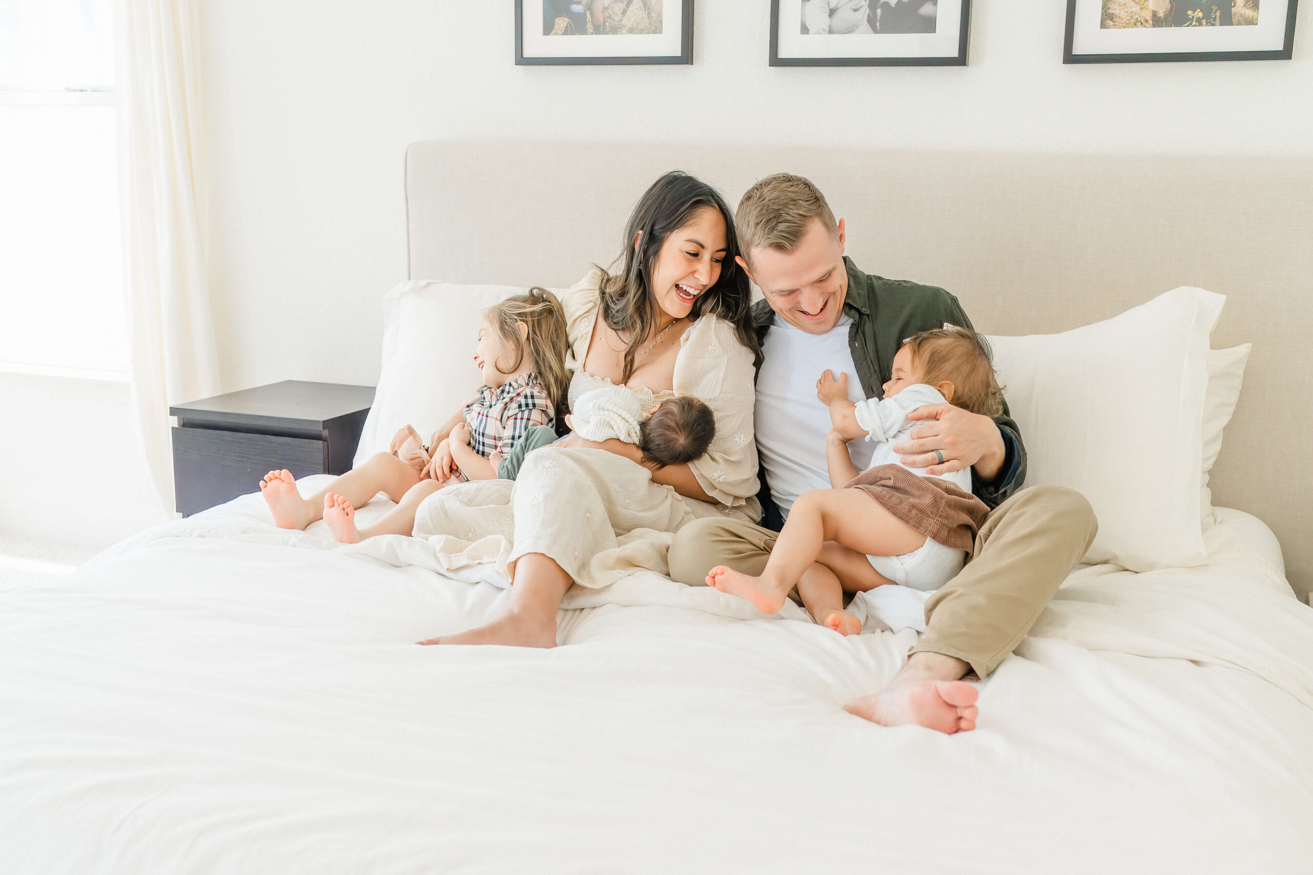 A happy mom and dad play with their two toddler daughters and newborn in their laps on a bed after meeting nannies in austin