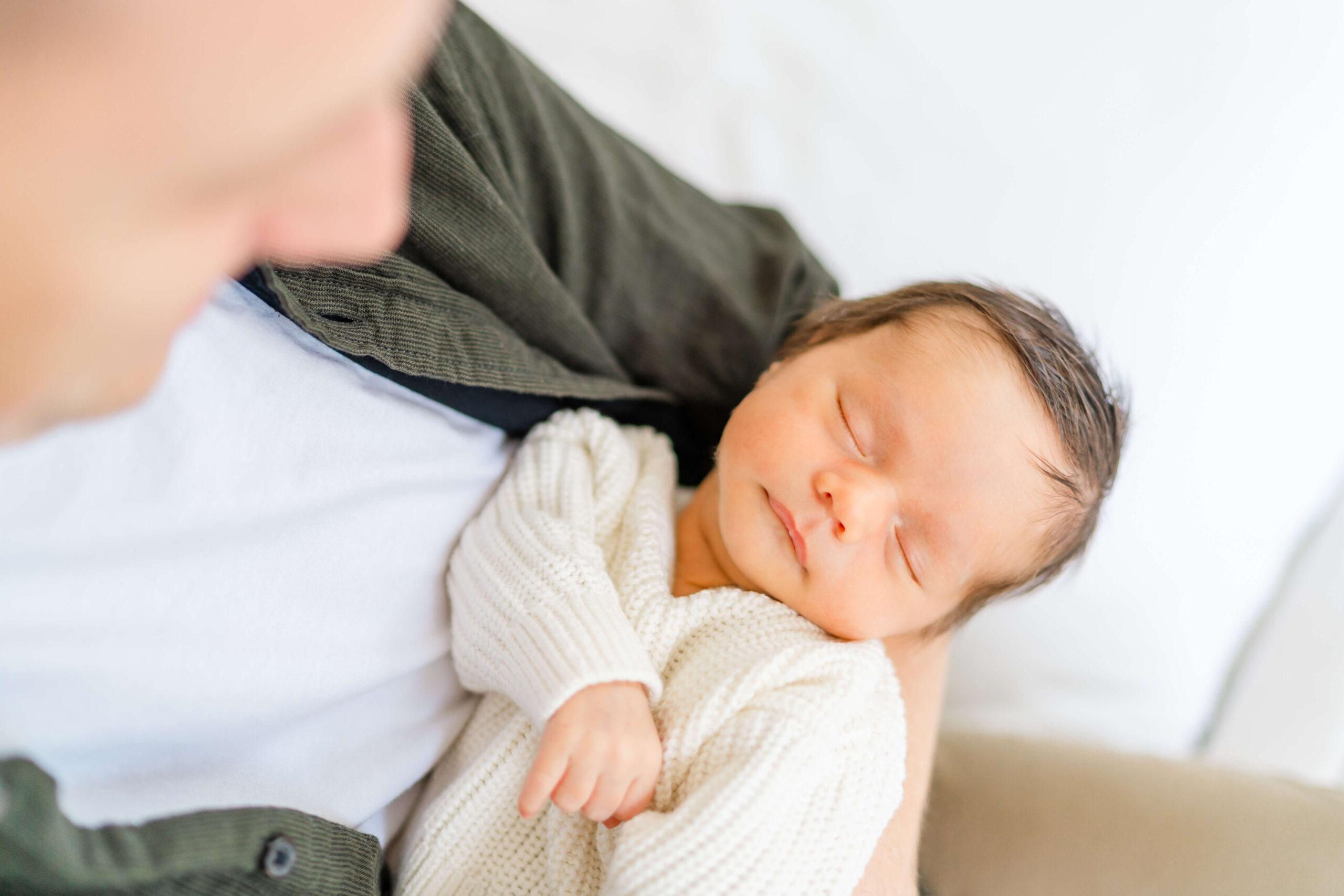 A newborn baby sleeps in dad's arms in a knit onesie before some infant swim lessons in austin