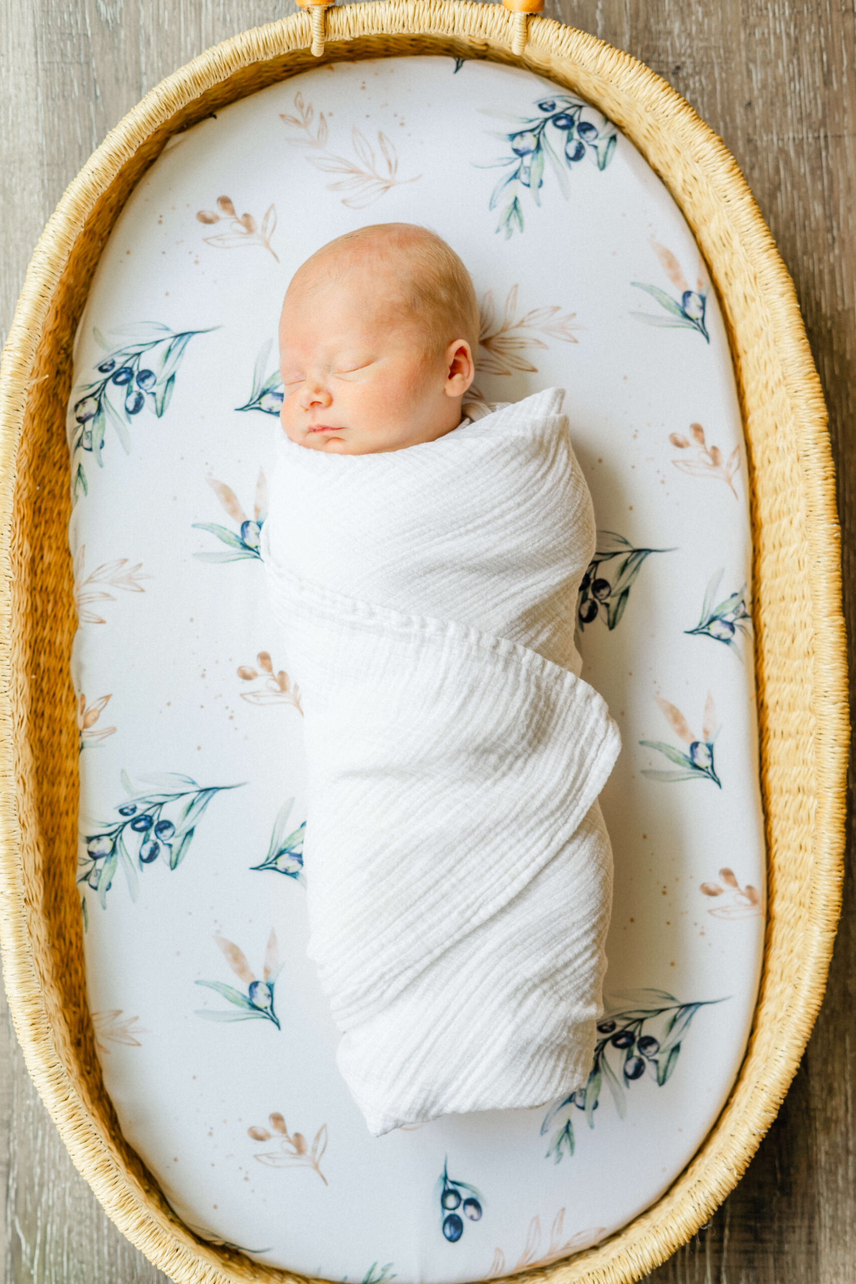 A newborn baby sleeps in a white swaddle in a woven basket on wood floor thanks to parenting classes in austin