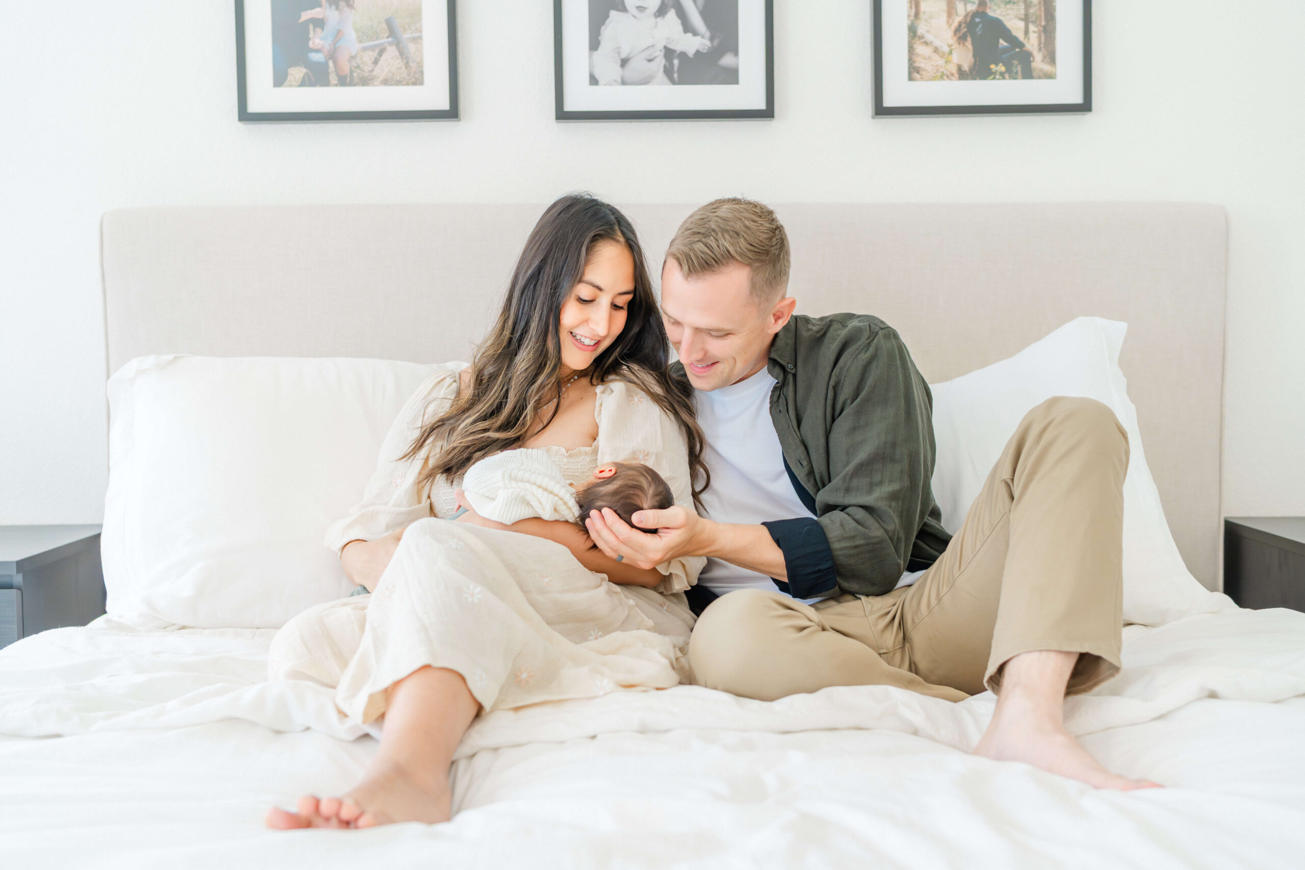 A mom and dad sit on a bed loving their newborn sleeping in mom's lap