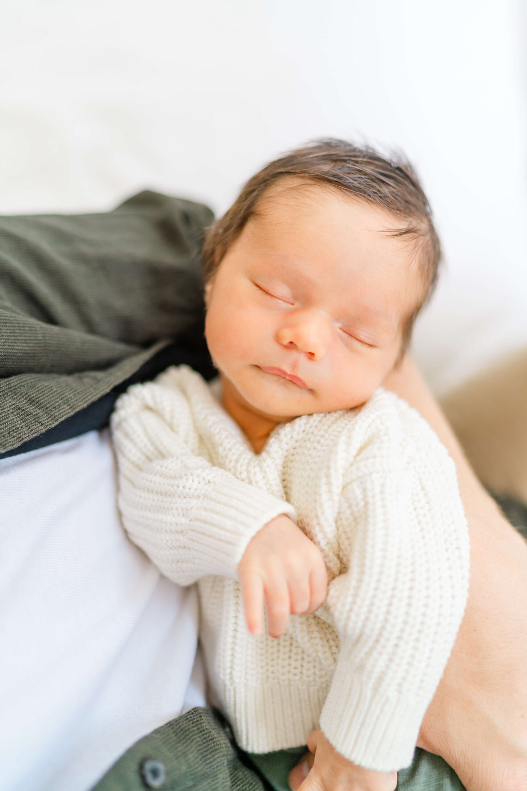 A newborn baby sleeps in a white knit sweater against dad's chest after visiting pediatric chiropractors in austin