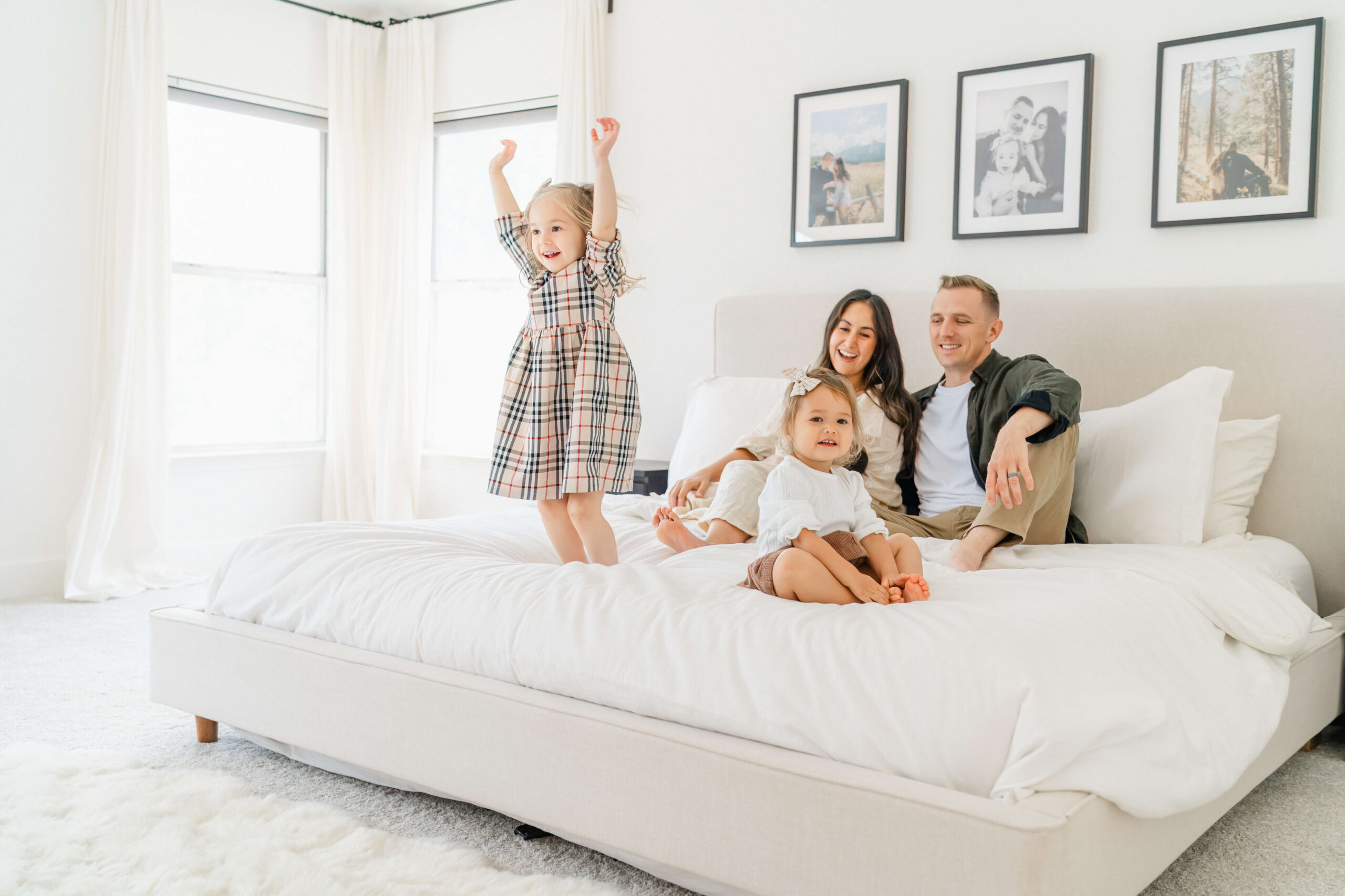 Toddler sisters jump and play on a bed as mom and dad sit behind them
