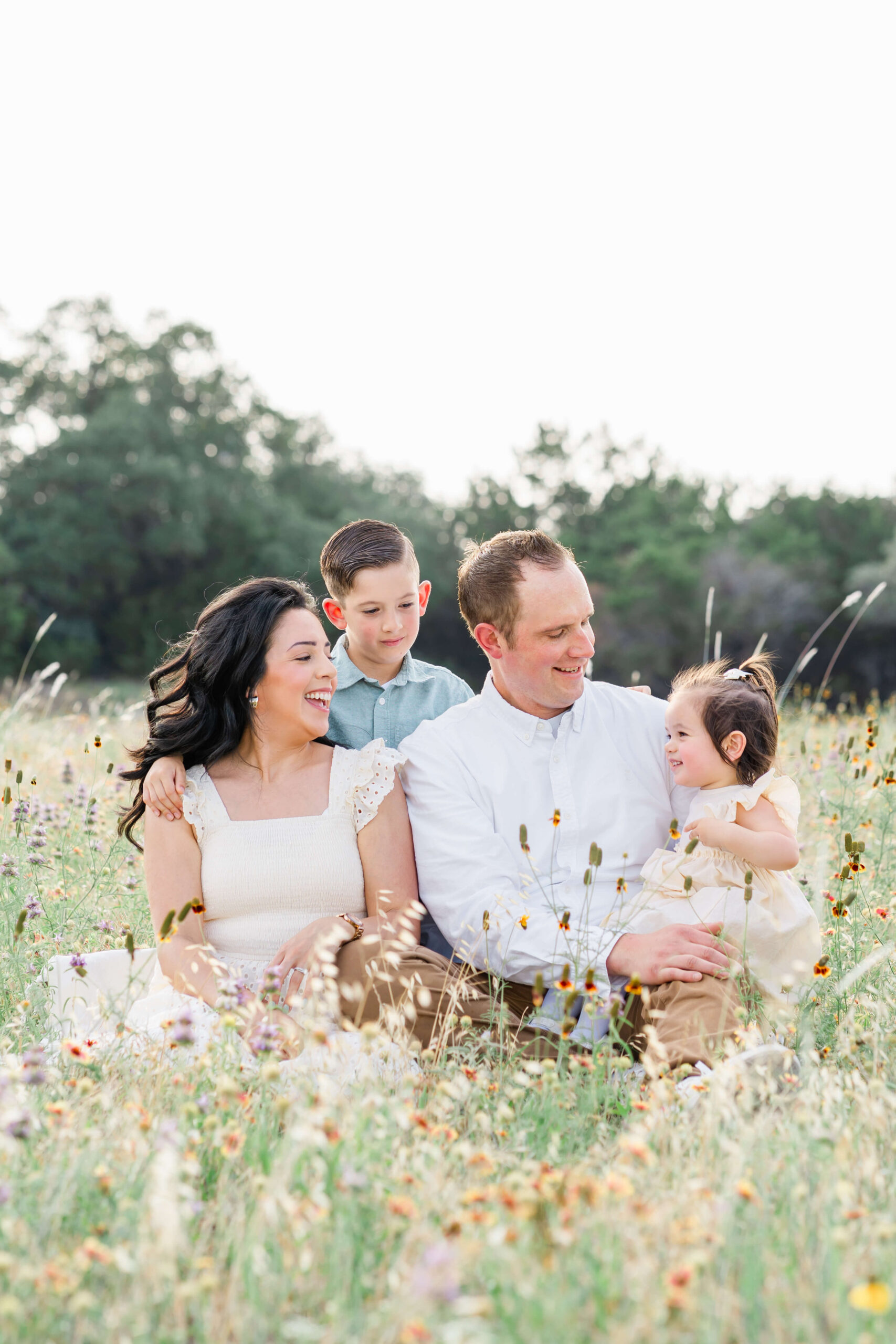 Happy mom and dad sit in a field of wildflowers with their toddler son and daughter after enjoying montessori schools in austin