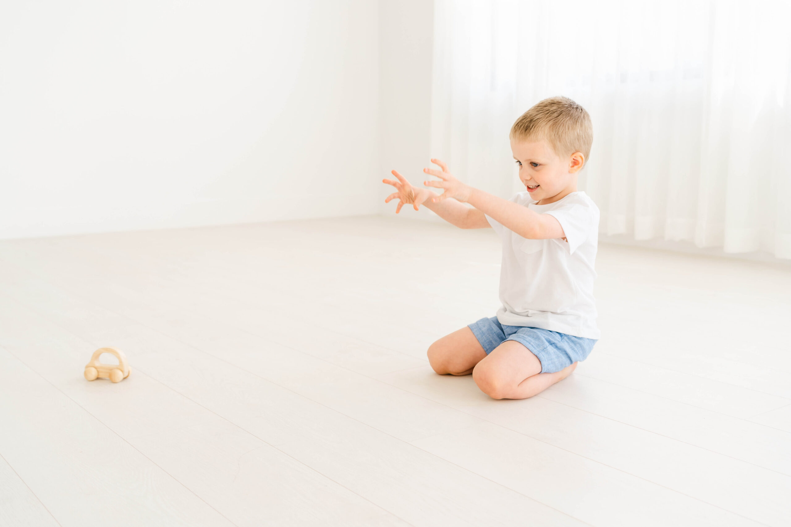 A toddler boy in a white shirt plays with a wooden toy in a studio after visiting preschools in austin