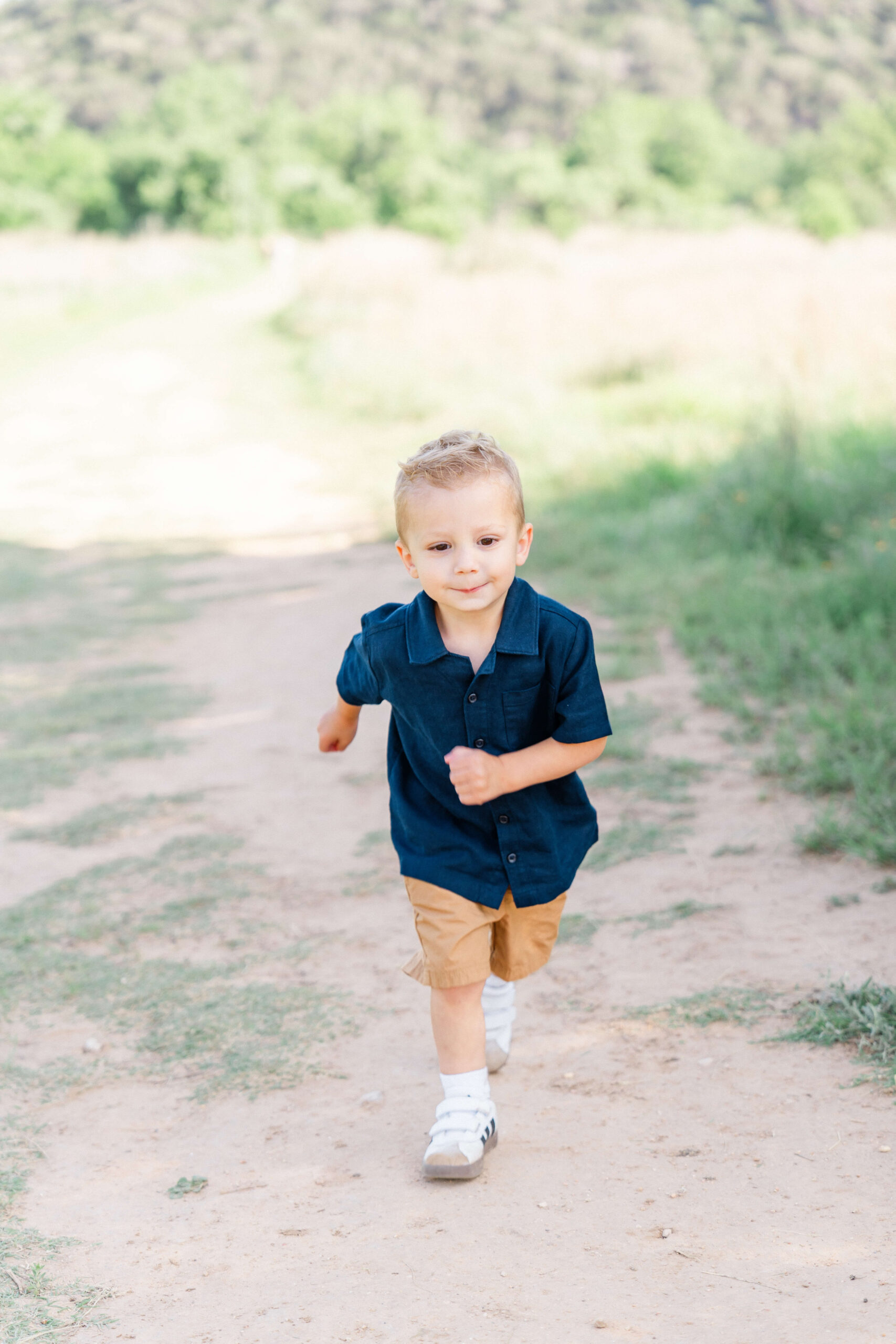 A toddler boy in a blue shirt runs in a park trail at sunset after visiting toy stores in austin