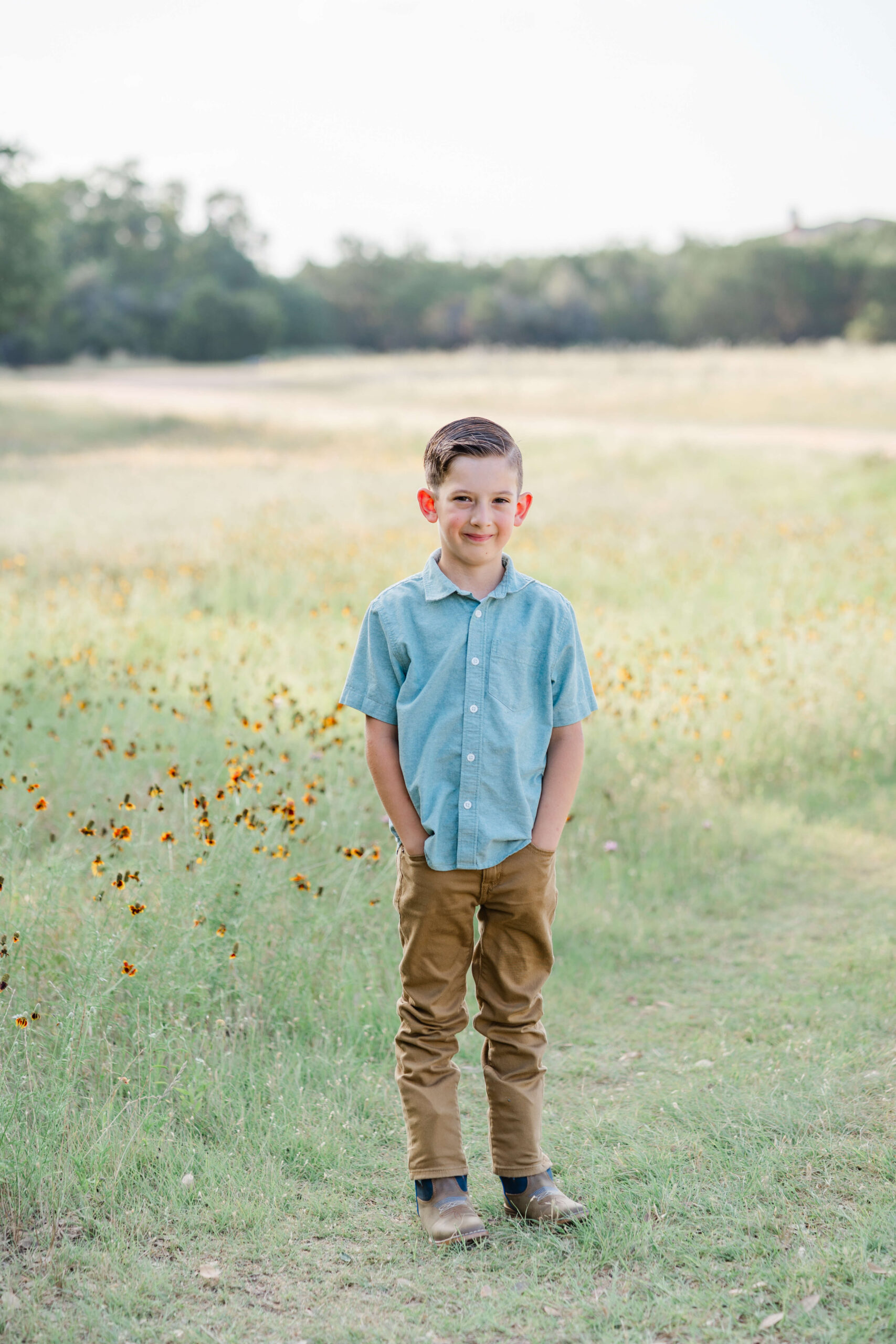 A young boy in a blue shirt stands in a trail through a field of wildflowers with hands in his pockets